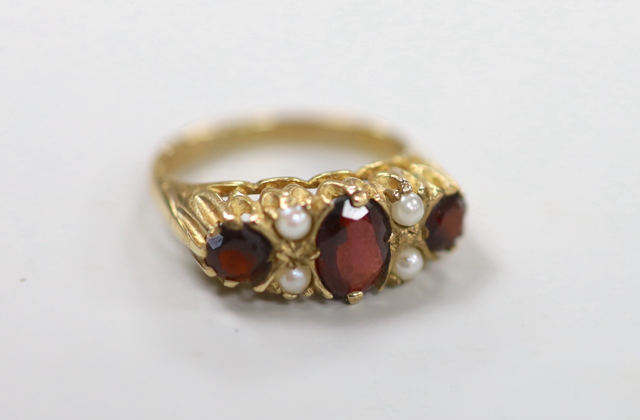 A 1970's 9ct gold, three stone garnet and four stone split pearl set half hoop ring, size K/L, gross weight 3.6 grams.